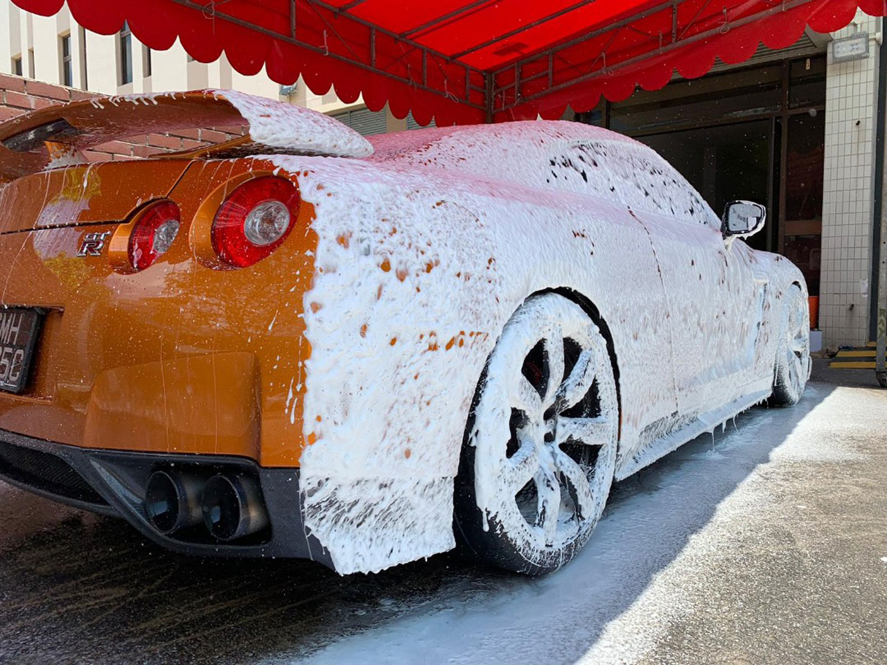 An orange sports car with a ceramic coating being washed in shade