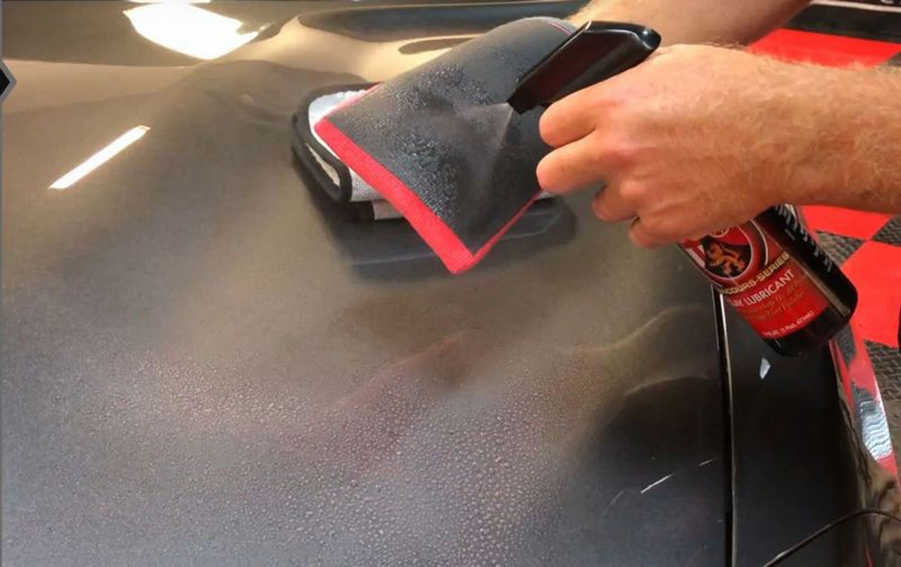 The clay mitt being sprayed with a clay lube spray before it's applied to a car.