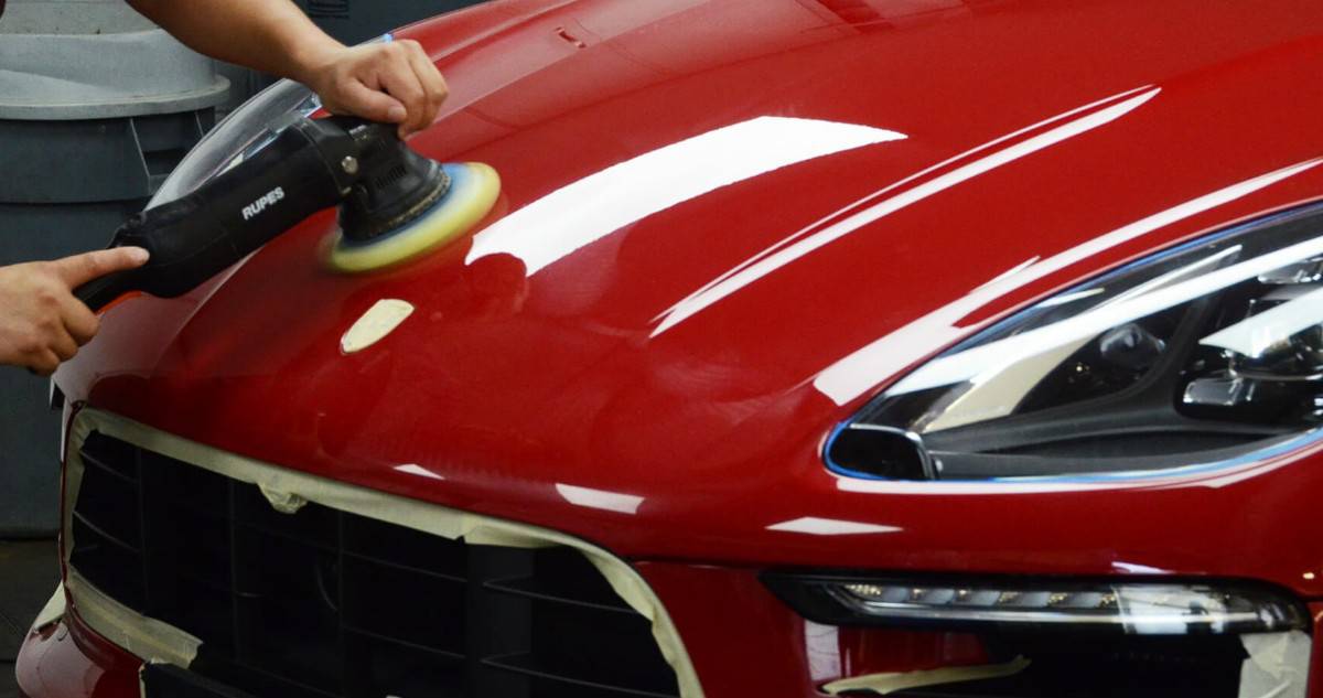 A professional detailer using an orbital polisher to remove scratches from car paint.